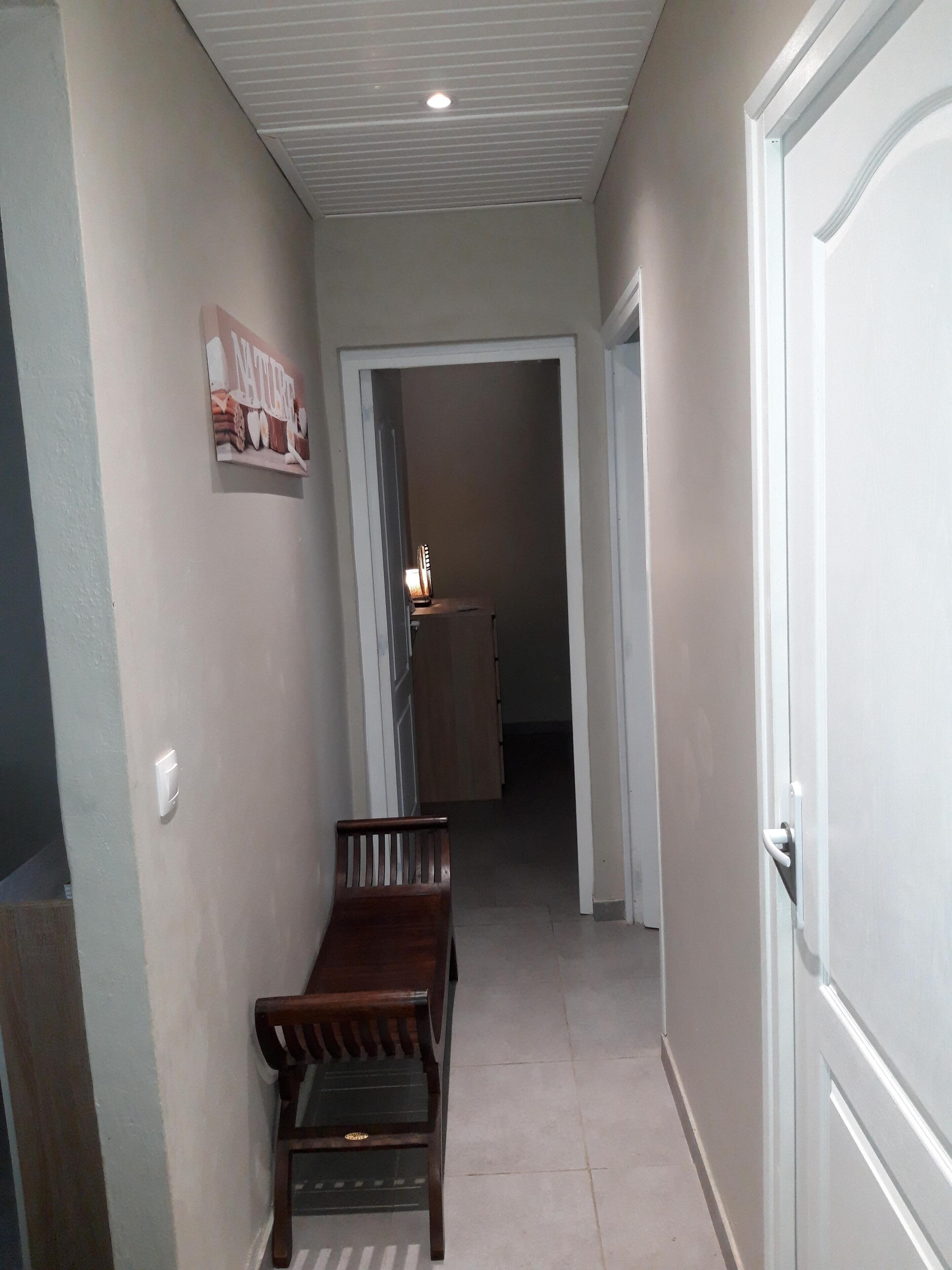 A hallway with a wooden bench, a door on the right, and a poster on the left.