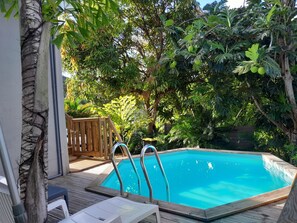 A swimming pool with wooden deck and lounge chairs, surrounded by lush greenery. - NEW SUITE COTTAGE F3 ANY COMFORT NEAR BEACH ANSE FIGUIER (Rivière-Pilote)
