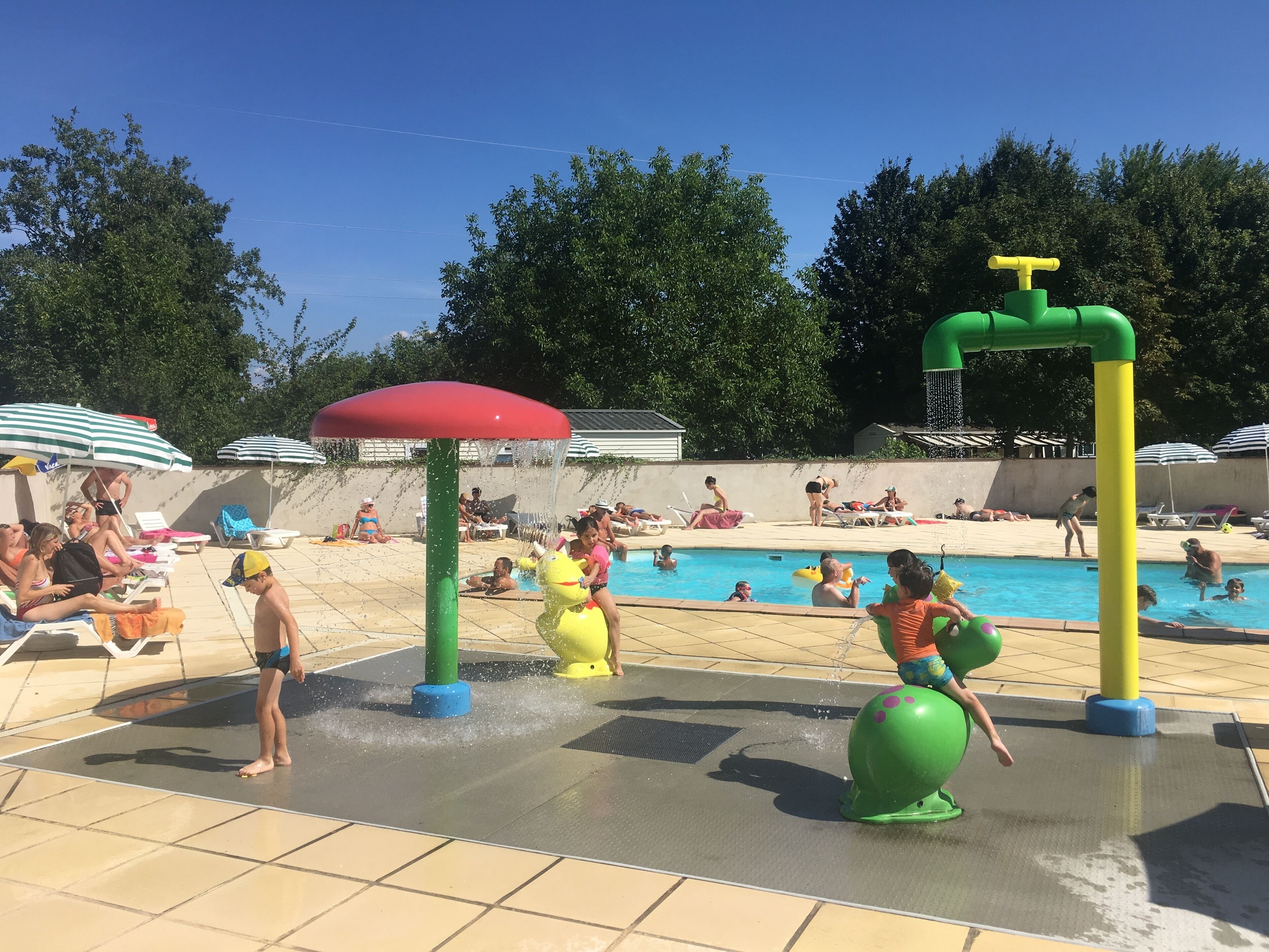 Un espace piscine doté de jeux d’eau et de chaises longues.