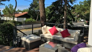 Zona relax all'aperto con mobili in vimini e cuscini, circondata da alberi e un cielo sereno.