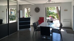 Un'area pranzo moderna con un tavolo grande e sedie, una sveglia al muro e vista all'esterno tramite una porta scorrevole.