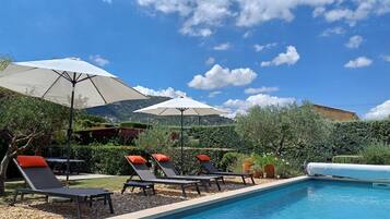 Un espace piscine doté de chaises longues et de parasols, entouré de verdure et avec une chaîne de montagnes en toile de fond.