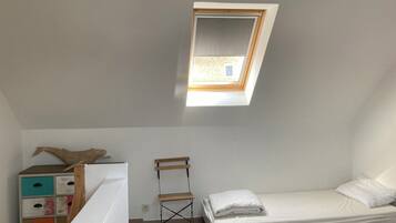 A small, bright room with a skylight, a bed, a wooden chair, and a colorful dresser.