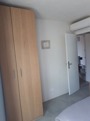 A bedroom with a wooden wardrobe, a white door, and an air conditioning unit on the wall.