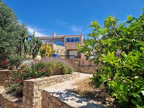A house with a stone facade, a garage, and a garden with various plants and cacti.