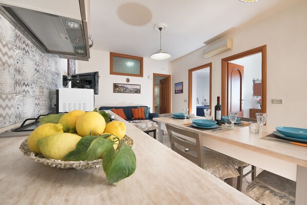 A modern kitchen with a central island, a dining area with a wooden table, and a living space with a sofa and a TV. - Panoramic Sea-View Villa in Amalfi – Authentic Local Escape (Amalfi)