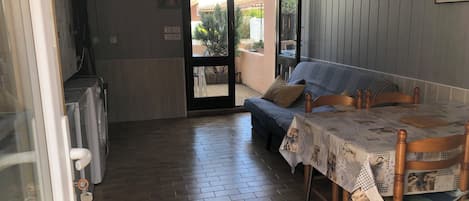 Un comedor con una mesa lista para dos, un sofá y vistas a un patio exterior a través de un ventanal.
