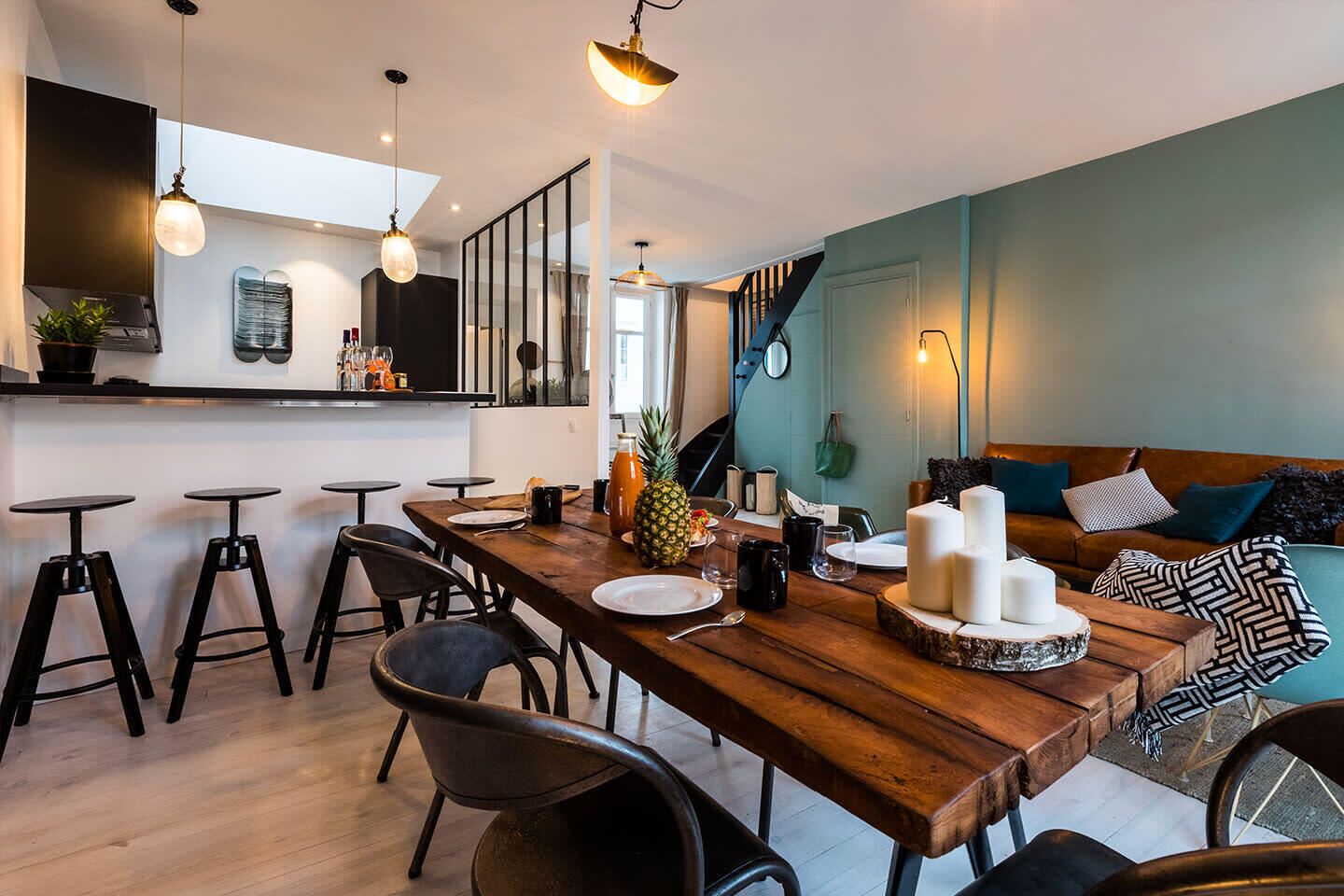 Une cuisine moderne avec une table à manger en bois, des tabourets de bar et un escalier menant à un niveau supérieur.