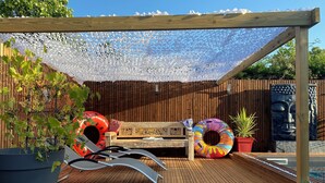 A wooden deck with a pergola, a bench, two inflatable rings, a potted plant, and a statue. - LARGE VILLA WITH SEA POOL PROMO LAST MINT (Messanges)