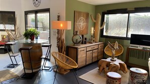 A modern living room with a glass dining table, wicker chairs, a wooden cabinet, and a television.