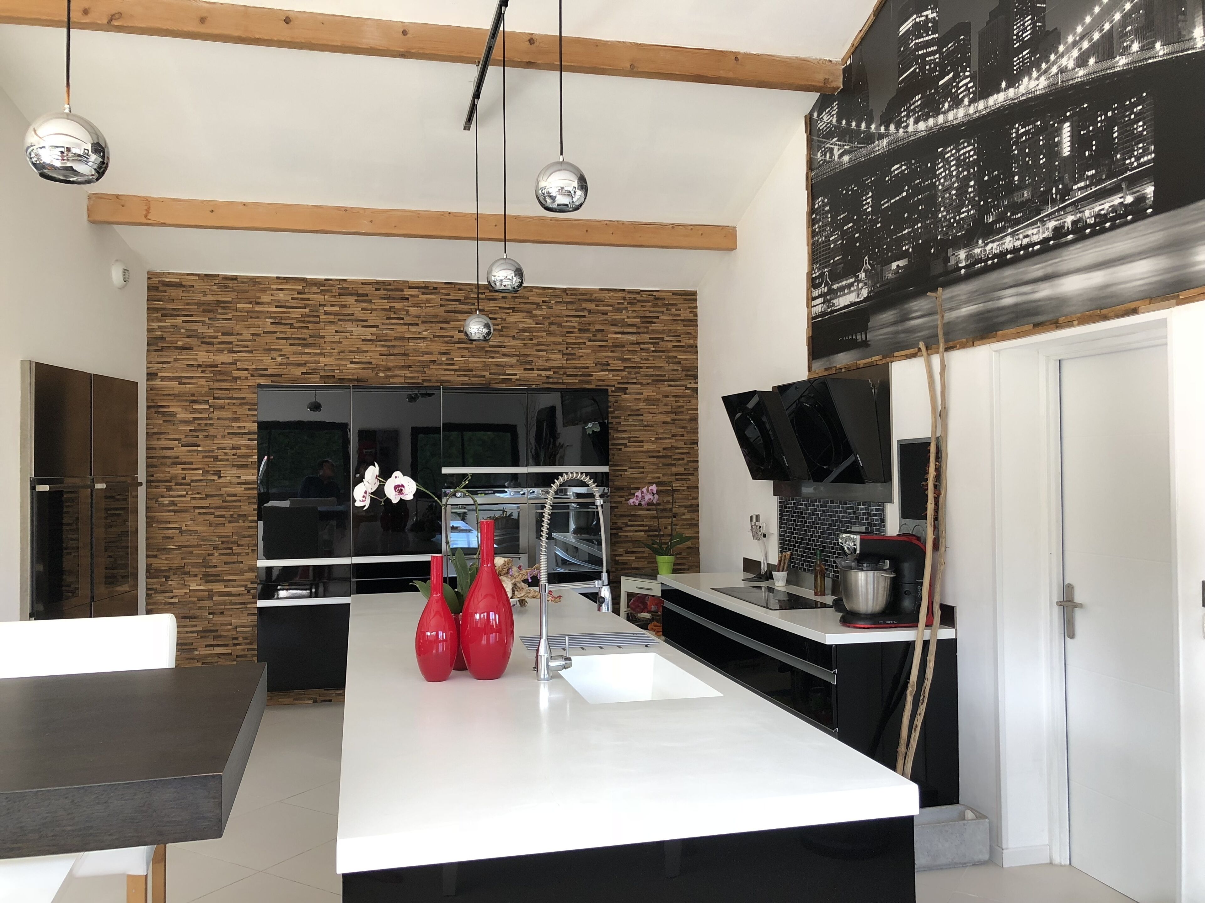Une cuisine moderne dotée d’un îlot central, de poutres en bois et de luminaires suspendus.