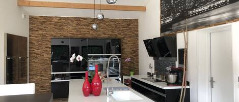Une cuisine moderne dotée d’un îlot central, de poutres en bois et de luminaires suspendus.