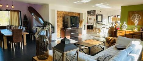 A modern living room with a sofa, coffee table, and a TV. There is a dining area with a table and chairs.
