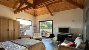 A spacious bedroom with a large bed, a wardrobe, a TV, and a balcony with a chair.
