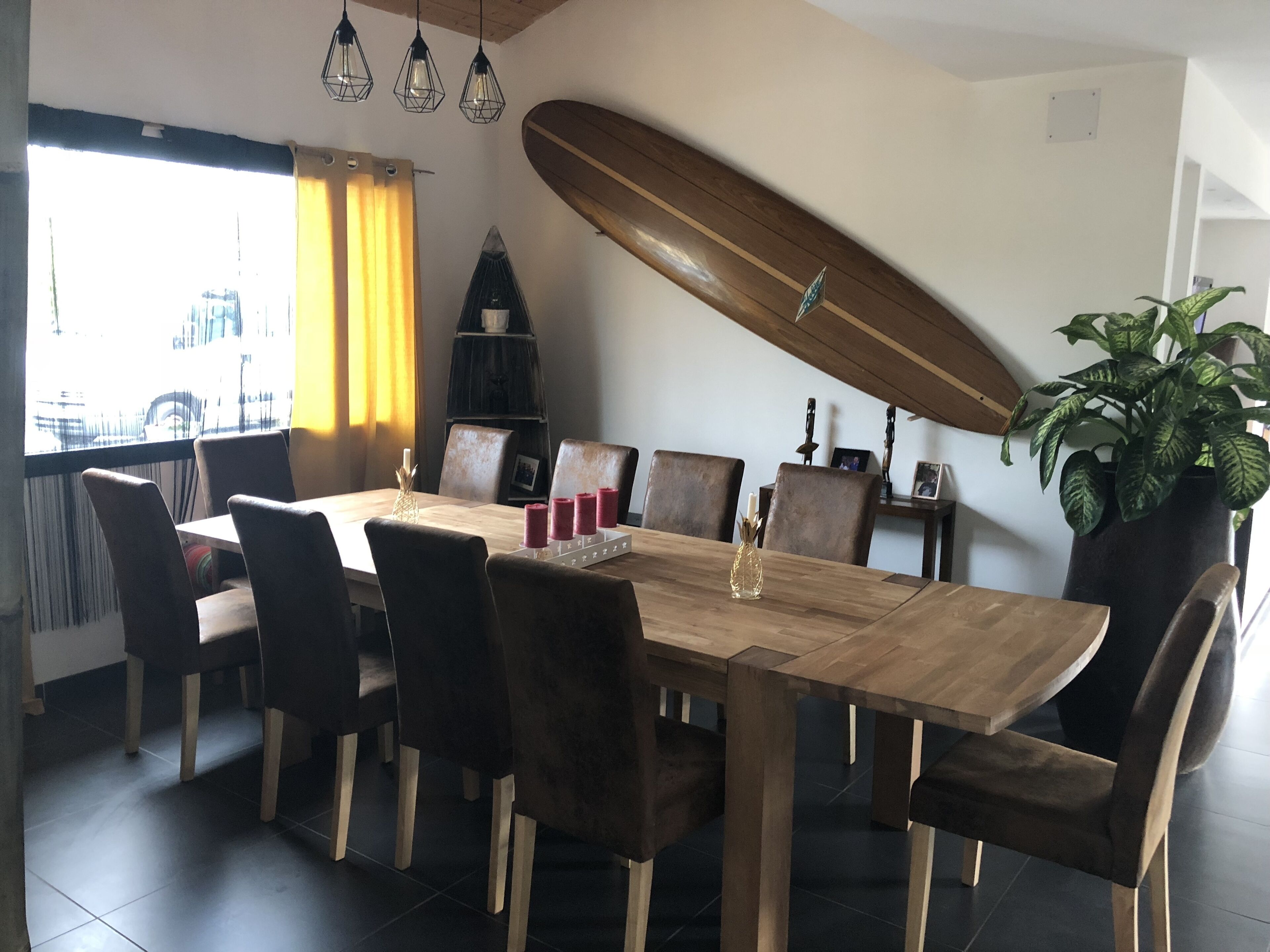 A dining area with a wooden table, dark chairs, and a surfboard mounted on the wall.