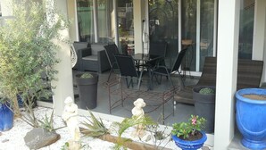 Eine überdachte Terrasse mit Gartenmöbeln, Blumentöpfen und einer Statue.