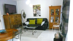 Ein Wohnzimmer mit Sofa, einem Esstisch mit Stühlen, einem Fernseher, einem Schrank und einer dekorativen Laterne.