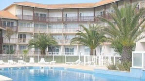 A hotel with a swimming pool, multiple balconies, and palm trees. - Appt classified 4 *, 2 swimming pools, free WIFI, terrace, bbq, edge of the marine lake (Vieux-Boucau-Les-Bains)