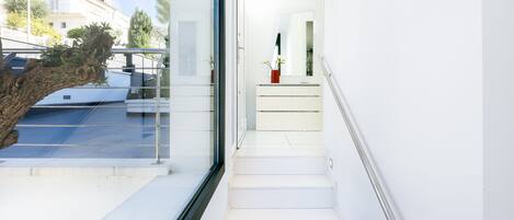 A modern staircase leading to a balcony with a glass railing, a potted plant on the landing, and a view of a building with a balcony.