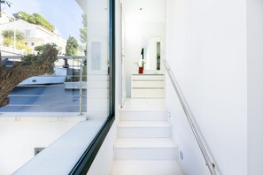 A modern staircase leading to a balcony with a glass railing, a potted plant on the landing, and a view of a building with a balcony.