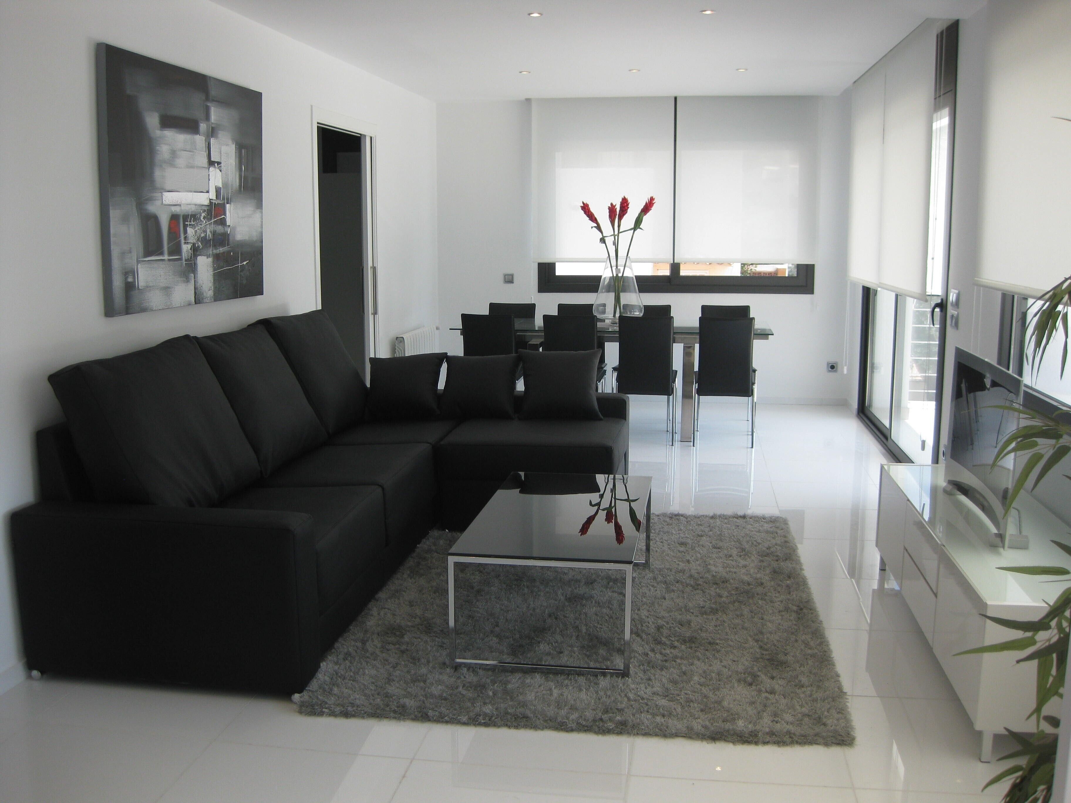 A modern living room with a black sectional sofa, a glass coffee table, and a dining area with a glass table and chairs.