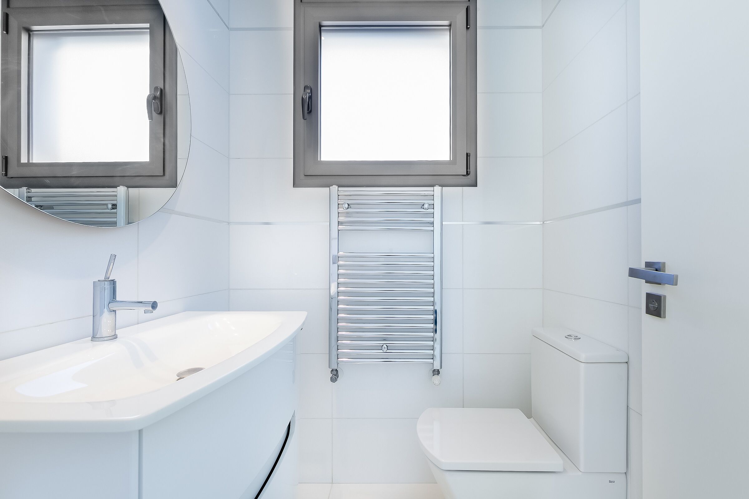 A modern bathroom with a white sink, a mirror, a window, and a toilet.