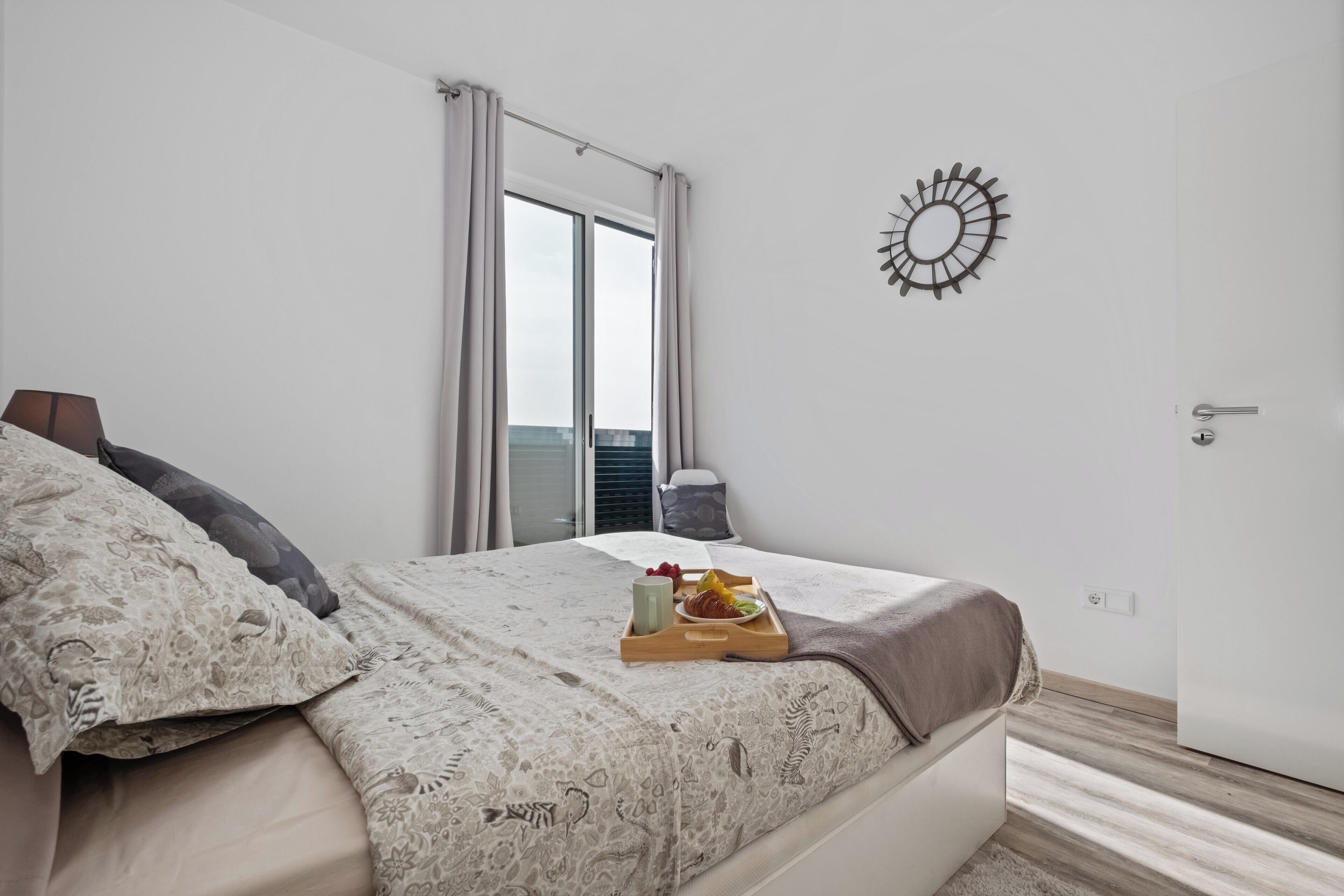 Un dormitorio con cama, una bandeja con alimentos para el desayuno, una ventana con cortinas y un adorno en la pared.