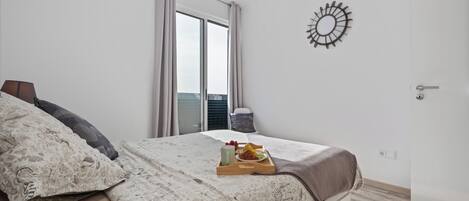 Un dormitorio con cama, una bandeja con alimentos para el desayuno, una ventana con cortinas y un adorno en la pared.