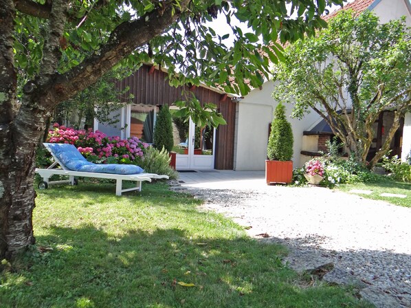 A garden with a white lounge chair, a gravel path, and a building with a wooden fence and a door.