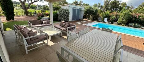 An outdoor patio with a pool, surrounded by greenery and a small shed.