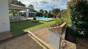 En trädgård med en pool, en täckt uteplats och en grill.
