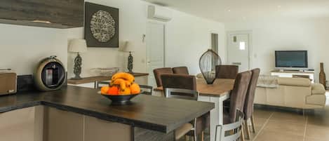 A modern kitchen with a central island, dining area with chairs, a sofa, and a TV in the living room.