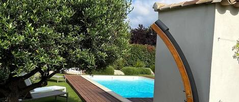 A pool area with a wooden deck, a small pool, and a white building with a curved wooden door.