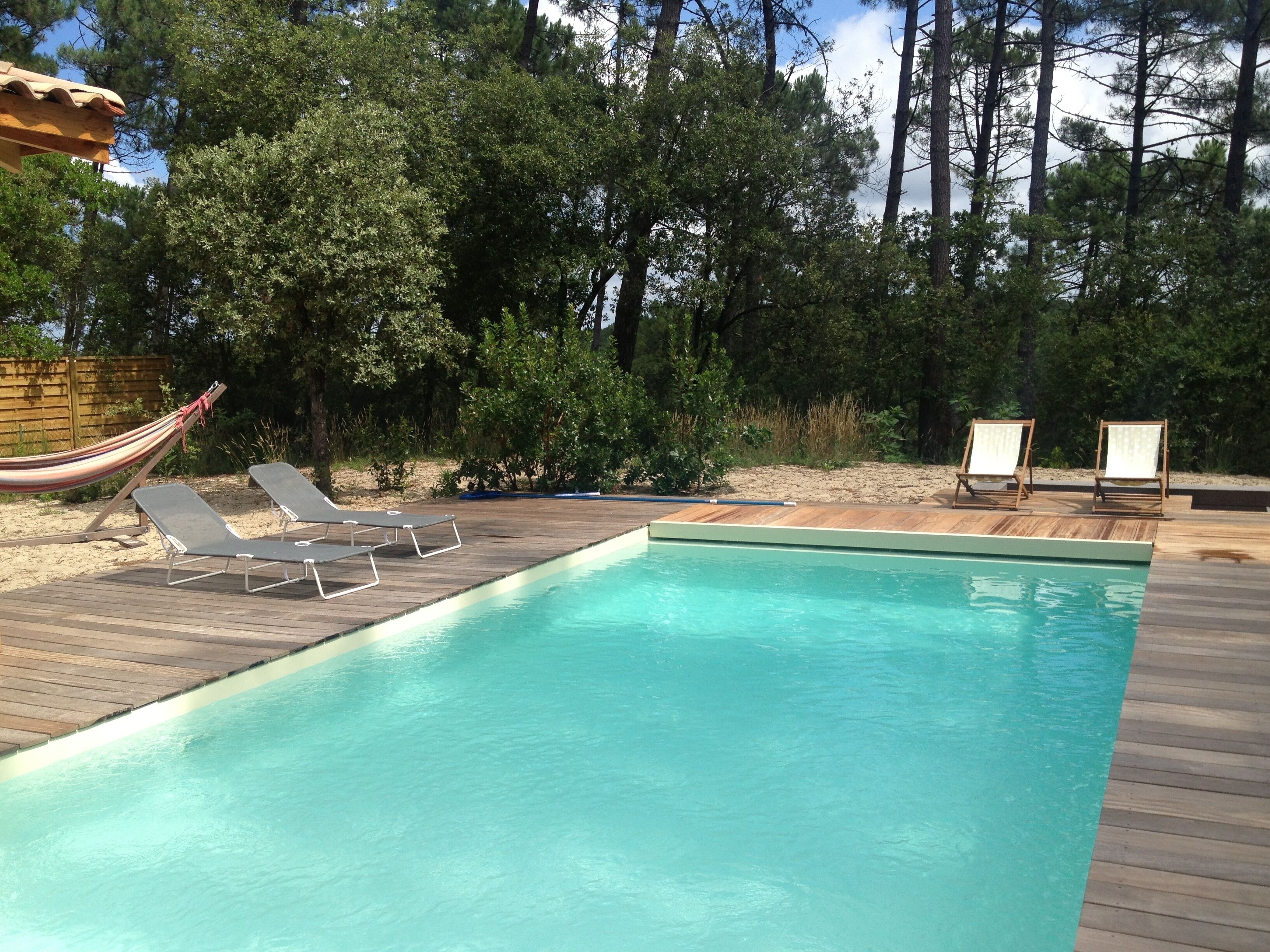 A rectangular swimming pool with a wooden deck, two lounge chairs, and a hammock.