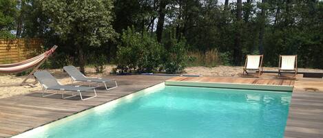 A rectangular swimming pool with a wooden deck, two lounge chairs, and a hammock.