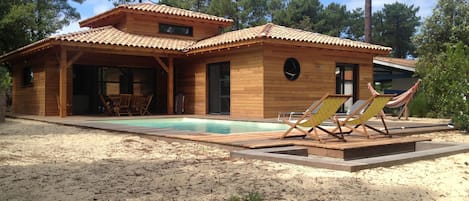 Una cabaña de madera con piscina, asientos exteriores y una hamaca.