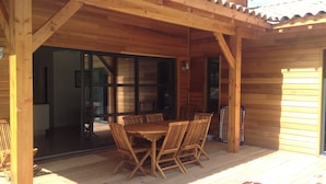 En træterrasse med et bord og stole, en pergola og en skydedør, der fører ind i et rum.