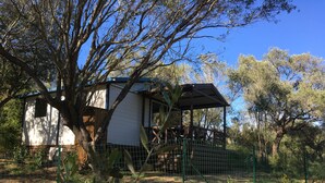 A white house with a wooden deck and a covered porch, surrounded by trees and a fenced garden. - Bungalow Philippi Maurea 5 (air-conditioned )300 meters from the beach. (Belvédère-Campomoro)
