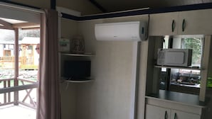 A compact room with a TV, air conditioning unit, and a microwave. - Bungalow Philippi Maurea 5 (air-conditioned )300 meters from the beach. (Belvédère-Campomoro)