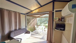 A room with a bed, a table, and a TV. There is a window with curtains, and a door leading to an outdoor area with a table and chairs. - Bungalow Philippi Maurea 5 (air-conditioned )300 meters from the beach. (Belvédère-Campomoro)