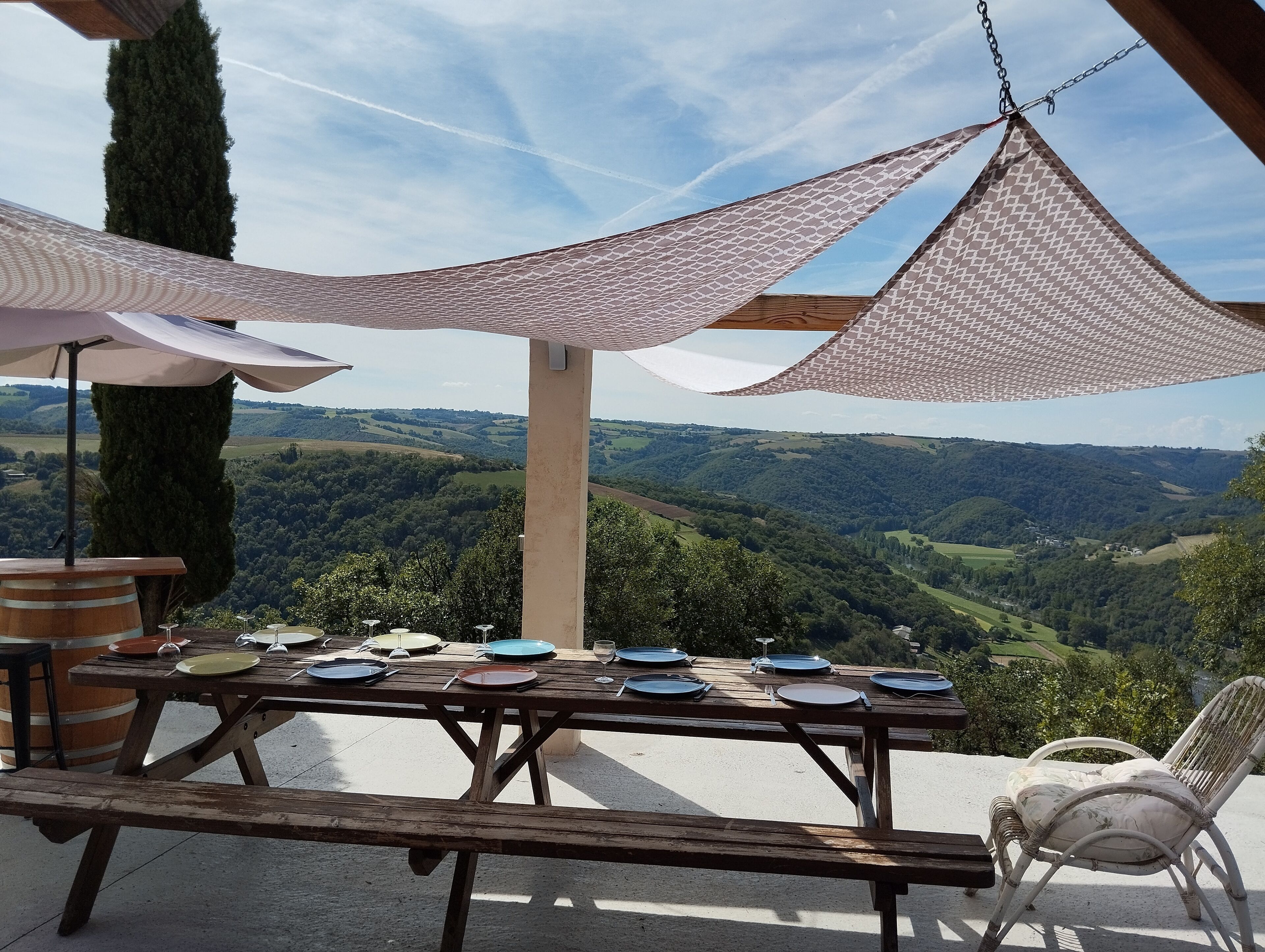 Ein Holztisch für ein Picknick mit Tellern und Besteck, vor einer malerischen Kulisse aus sanften Hügeln und blauem Himmel.