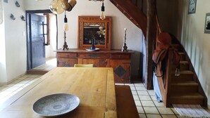 A dining area with a wooden table and chairs, a decorative mirror, and a staircase leading to an upper level. - Gîte 12 pers, pétanque court, swimming pool : week from july 11th to 18th free ! (Courris)
