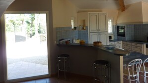 Une cuisine dotée d’un grand îlot central, de deux tabourets de bar et offrant une vue sur l’extérieur.