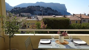 A balcony with a table set for two, overlooking a mountainous landscape with buildings in the background.