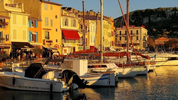 A marina with boats docked, surrounded by colorful buildings with shops and restaurants.