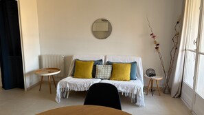 A cozy living room with a sofa, a round mirror, a small table, and a radiator.
