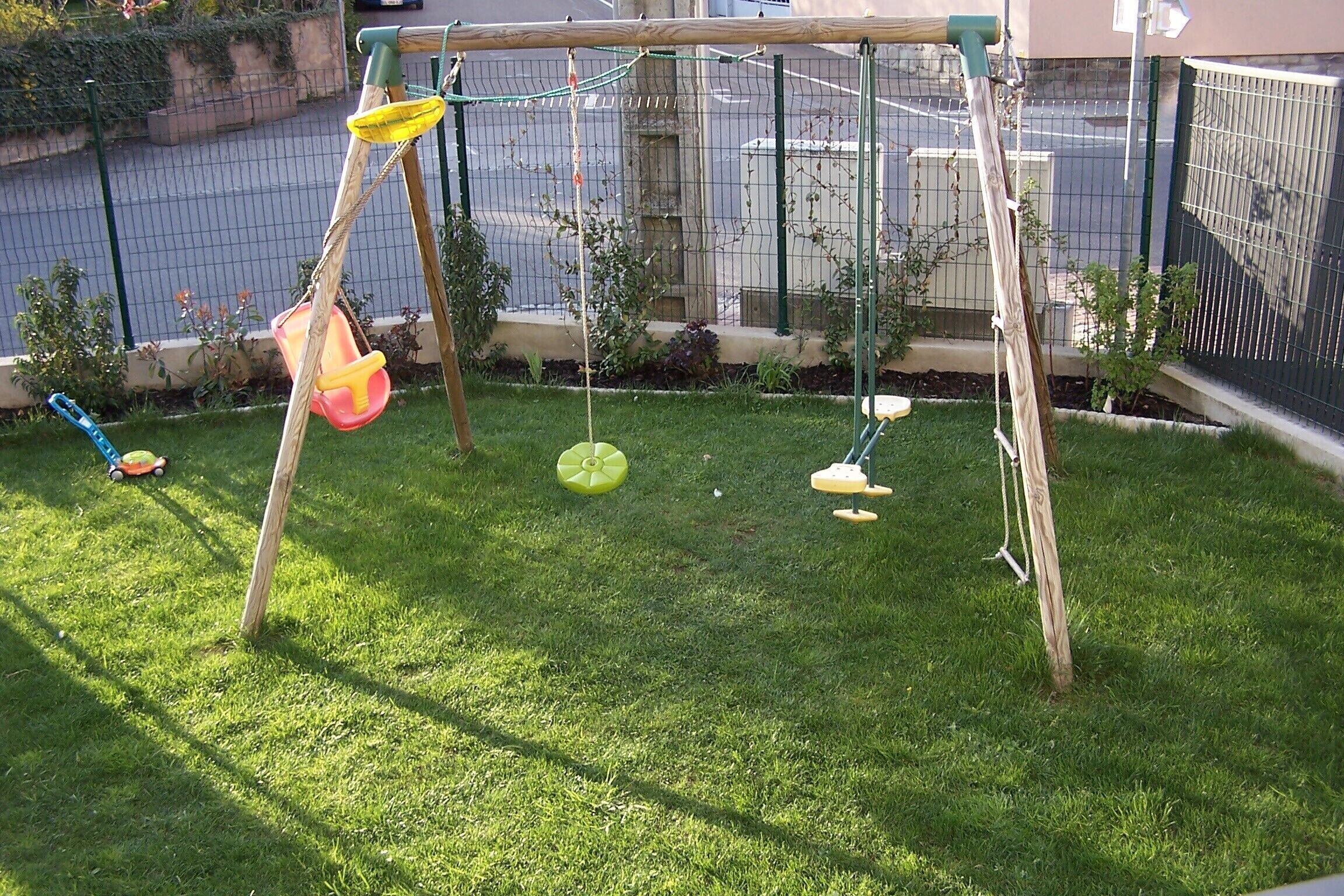 A swing set with a netted enclosure, a small garden area with grass, and a fence in the background.