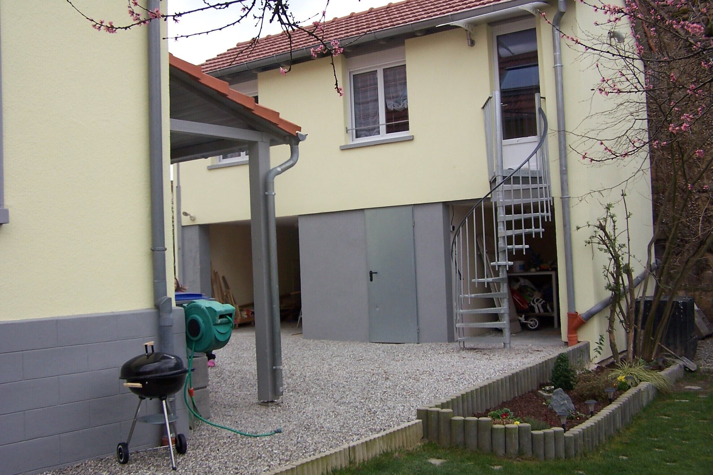 Ein Haus mit überdachter Terrasse, Grill und kleinem Garten.