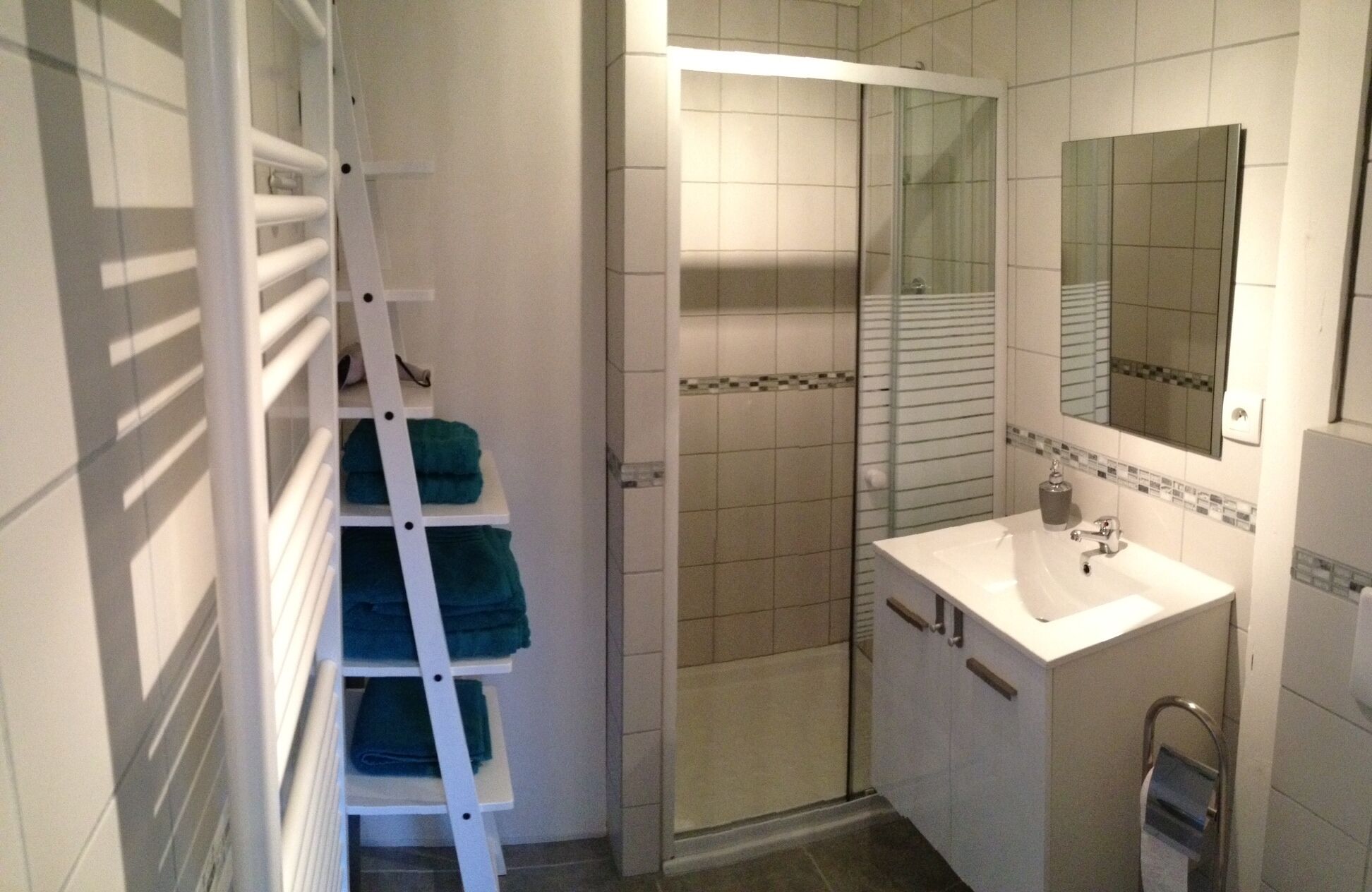 A bathroom with a white sink, a mirror, a shower, and a towel rack with folded towels.