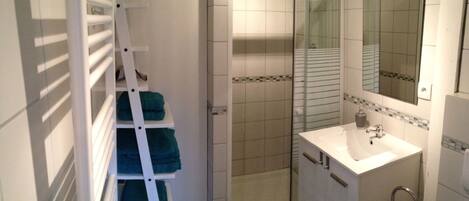 A bathroom with a white sink, a mirror, a shower, and a towel rack with folded towels.